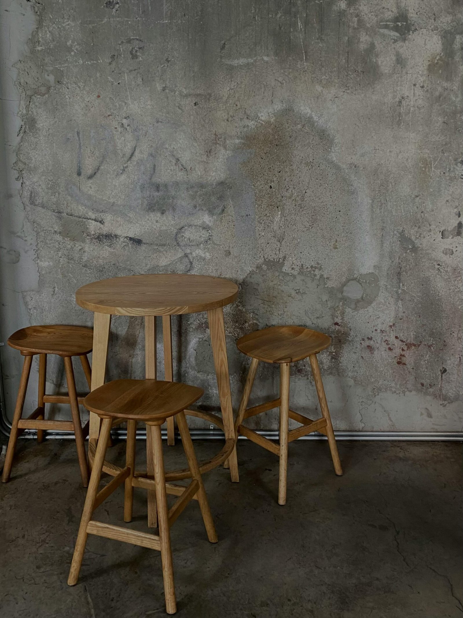 Wooden stools and a table set against a rustic concrete wall in an industrial-style room.